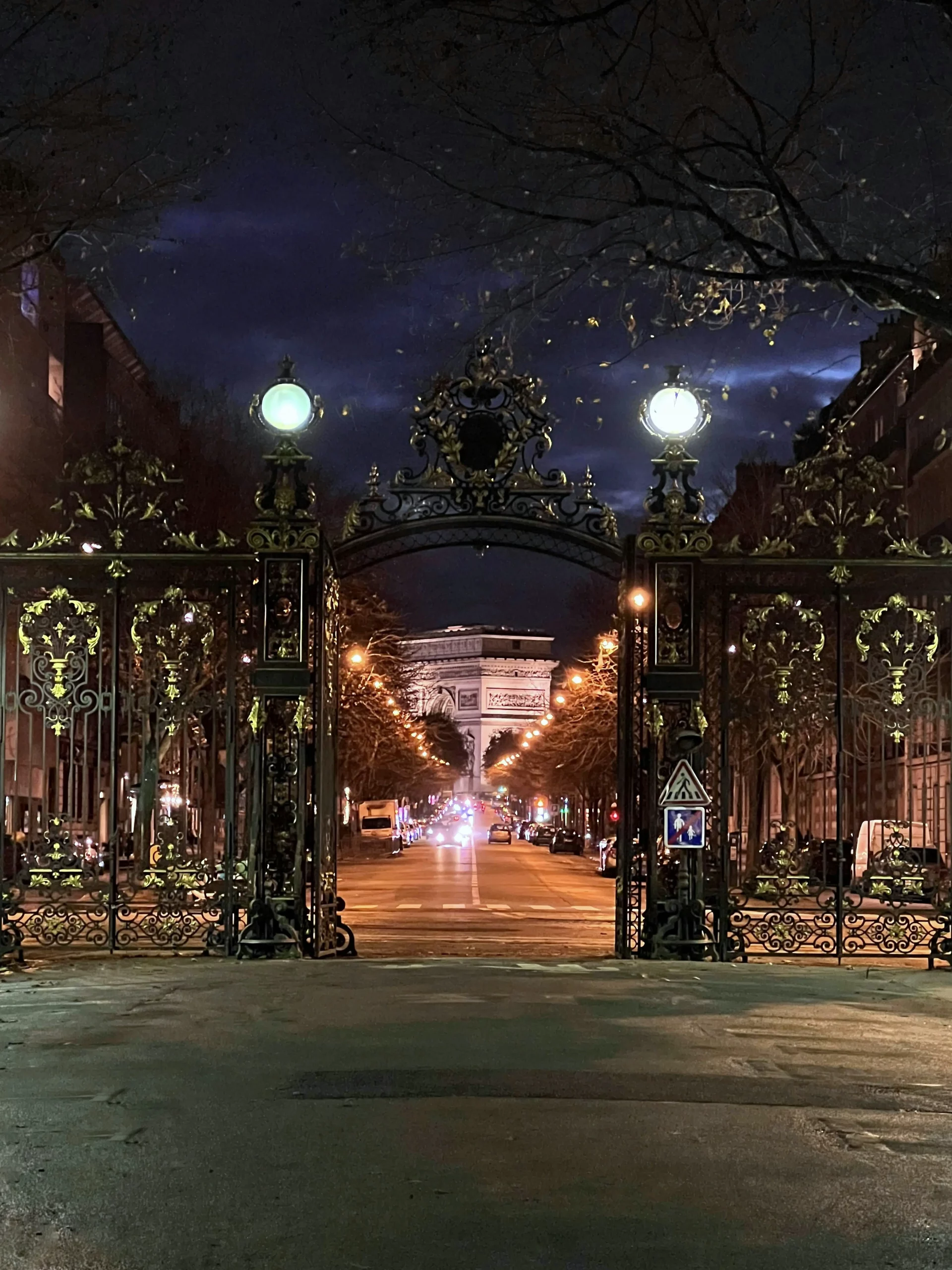 Porte du Parc Monceau illuminée la nuit dans le 17ᵉ arrondissement, avec vue sur l’Arc de Triomphe